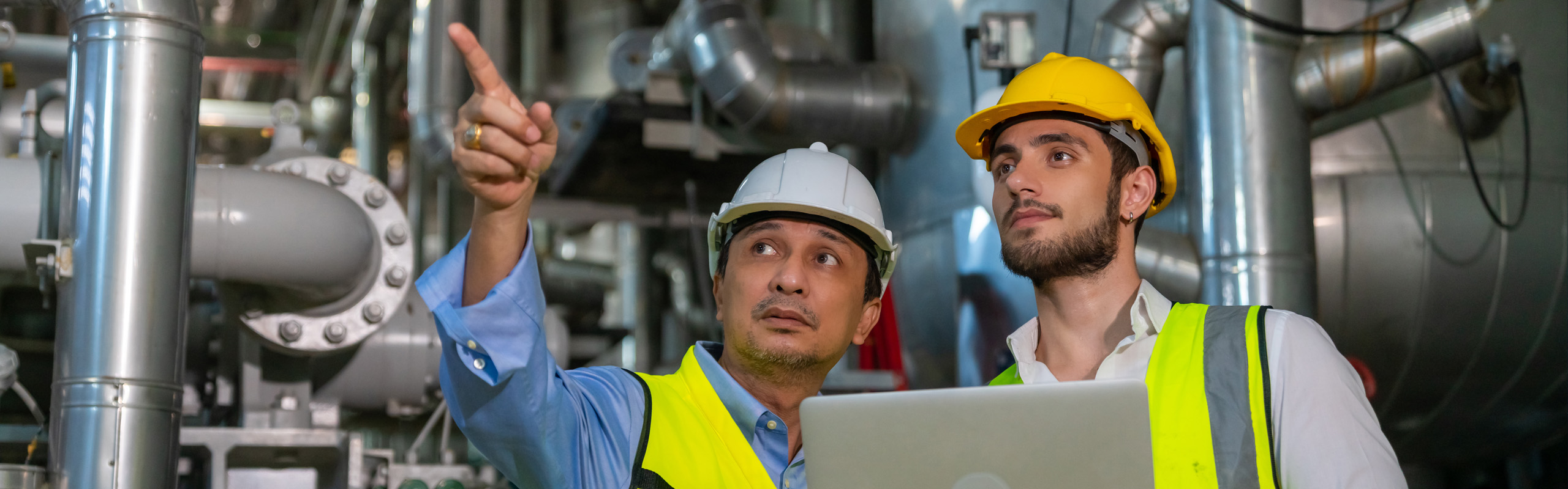 Zwei Männer mit Schutzhelmen zeigen auf etwas außerhalb des Bildes.