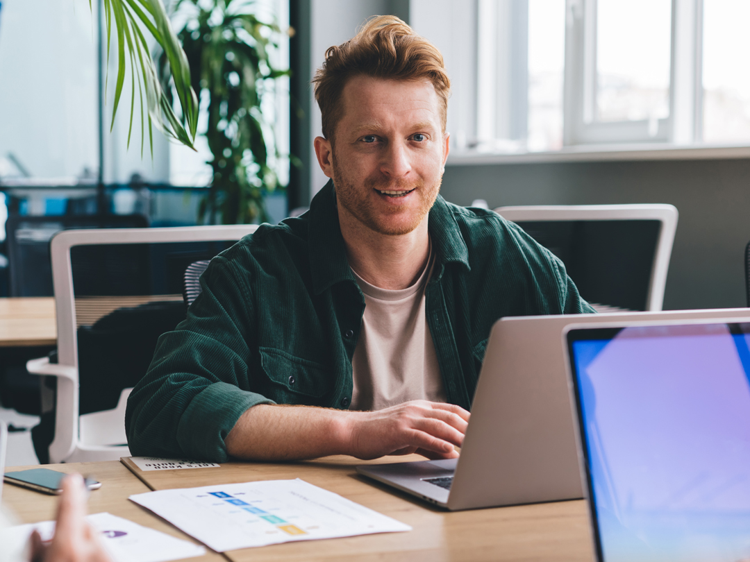 Mann sitzt an einem Schreibtisch und arbeitet mit einem Laptop in einem Büro.