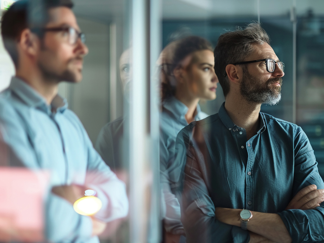 Mann mit Brille und Bart steht vor einer transparenten Wand.
