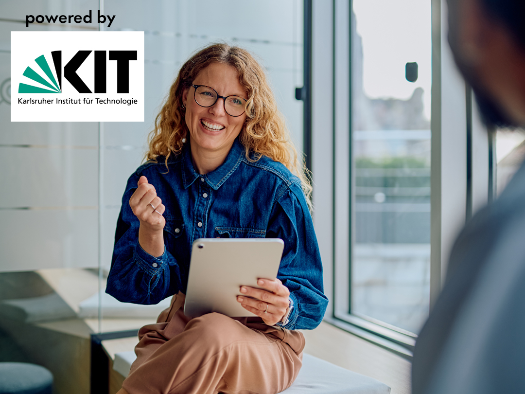Smiling woman with curly hair and glasses holds a tablet in a bright office; KIT branding appears in the corner.