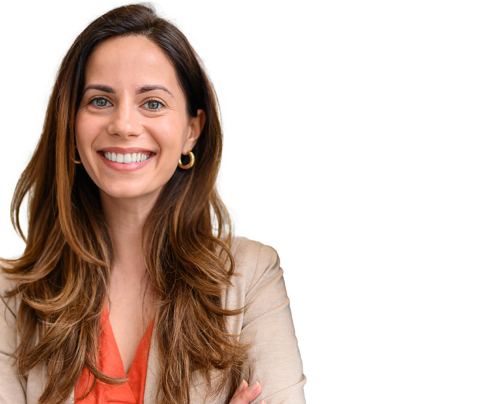 Smiling woman with long brown hair and hoop earrings leaning against a grey pillar outdoors, wearing a coral top and beige blazer.